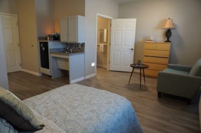 A cozy resident room with a bed, dresser, and seating