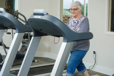 An elderly woman walking on a treadmill in a gym area
