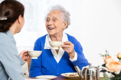 An elderly woman enjoying tea with a caregiver