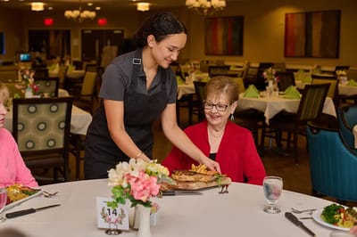 Masonic Village At Burlington, Nursing Home in Burlington, NJ — Server presenting meal to smiling resident at dining table