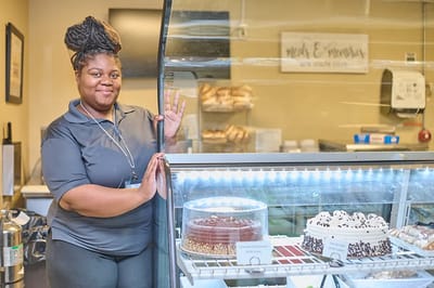 Masonic Village At Burlington, Nursing Home in Burlington, NJ — Woman smiling next to a dessert display case