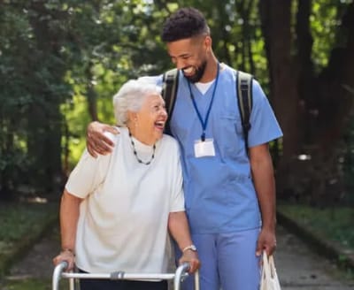A caregiver assisting a resident outdoors, both smiling