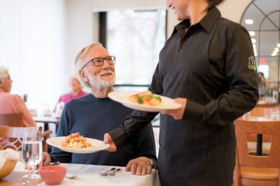 A staff member serving a meal to a resident in a dining area
