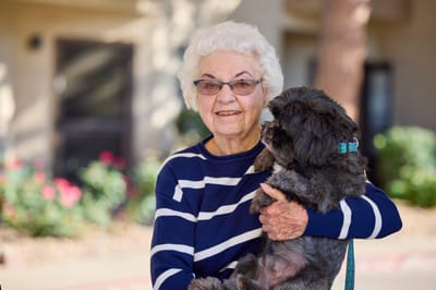 Senior resident holding a small dog in a garden area