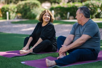 Two seniors stretching on mats in a green outdoor space