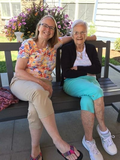 Two women sitting on a bench in a garden area