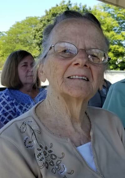 An elderly woman smiling at an outdoor gathering