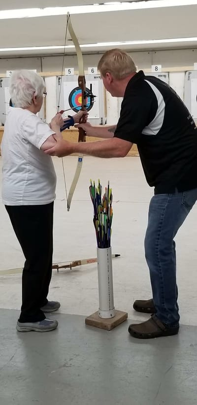 An instructor guiding a resident in archery practice