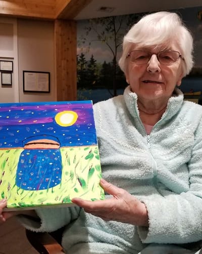 Resident showcasing a colorful painting in activity room