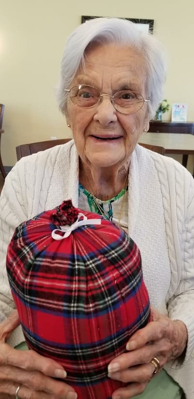 An elderly woman in a cozy interior holding a wrapped gift.