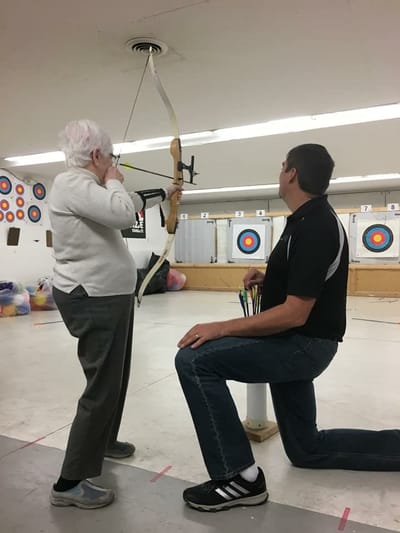 Senior resident practicing archery with staff assistance
