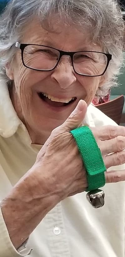 Resident smiling and giving a thumbs up with a bell on her hand