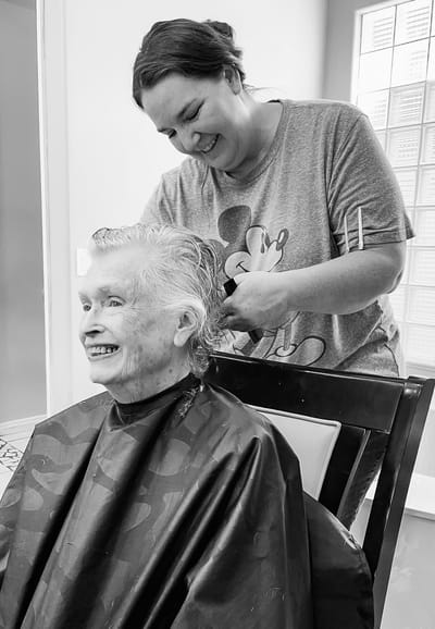 A resident receiving a haircut from a staff member in a bright room