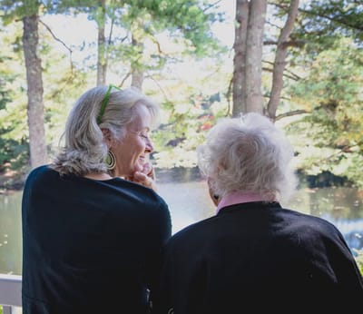 Two women enjoying a serene outdoor view by a pond