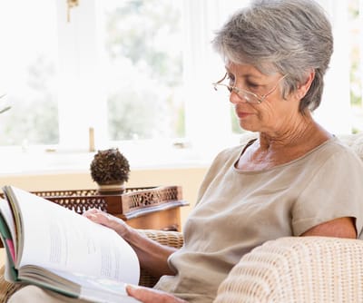 Senior reading a book in a cozy chair indoors