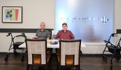 Two elderly men seated at a table in a common area