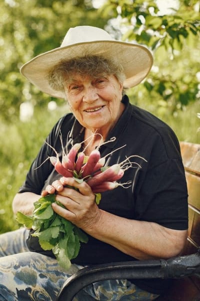 Resident smiling outdoors holding freshly harvested vegetables