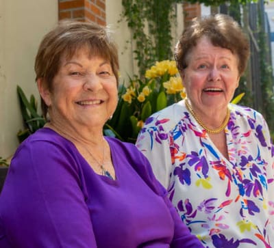 Two smiling women sitting in a garden area