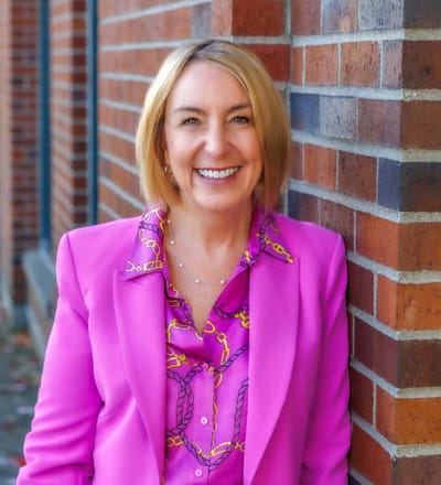 A woman smiling in a pink blazer, outdoors