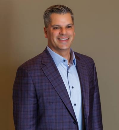 A smiling man in a blazer against a neutral backdrop