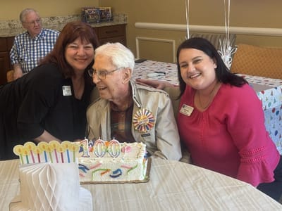 Residents celebrating a 100th birthday with cake and staff
