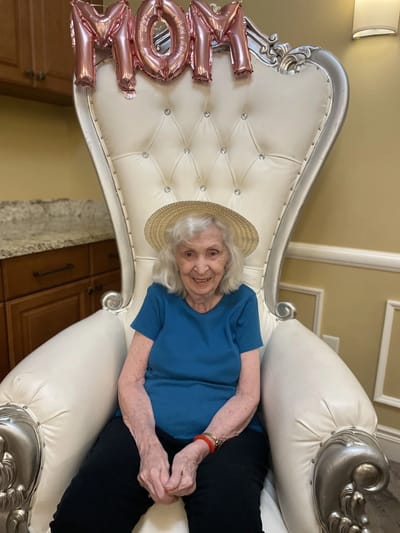 A resident celebrating with a 'Mom' balloon in a grand chair