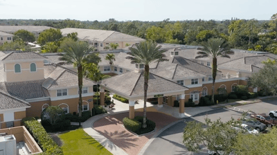 Aerial view of a senior living facility with gardens and palm trees