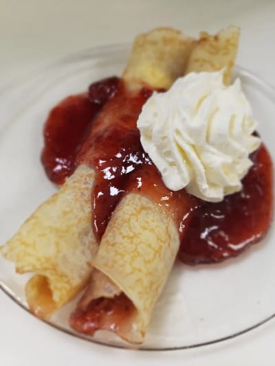 Dessert of crepes with strawberry sauce and whipped cream