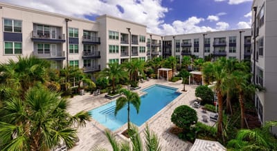 Outdoor pool area surrounded by palm trees and apartments