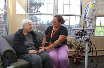 A caregiver taking blood pressure of a resident in a cozy room