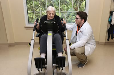 Senior resident using exercise equipment with staff assistance