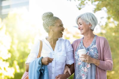Two women laughing and walking in a green outdoor area
