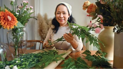A woman arranging flowers at a table surrounded by plants