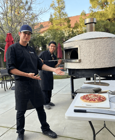 Two staff members presenting a pizza outdoors