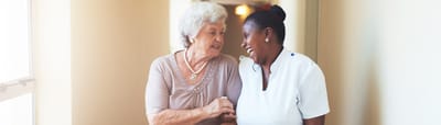 Meadowcrest – Middletown, Assisted Living in Middletown, DE — A caregiver and a resident smiling together in a hallway