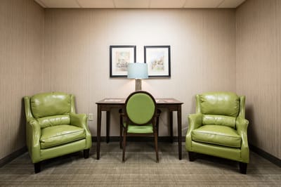 Cozy seating area with green chairs and a desk.