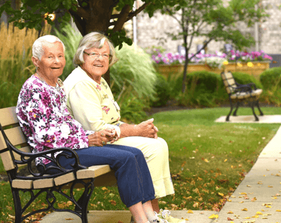 Two smiling women sitting on a bench outdoors.