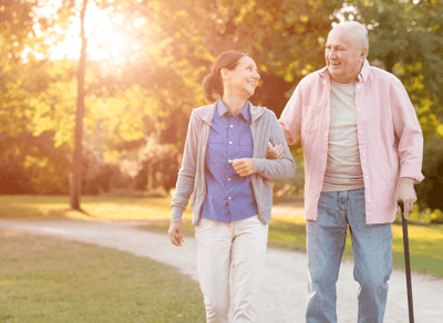 A caregiver walking with a resident in a sunlit park.