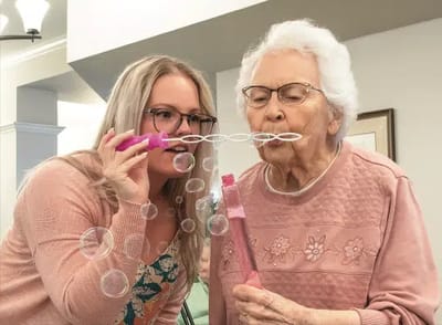 Senior resident enjoying bubbles with staff member.