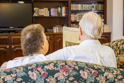 Two residents reading a newspaper on a couch.