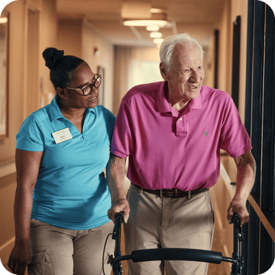 Staff assisting an elderly resident in a hallway.