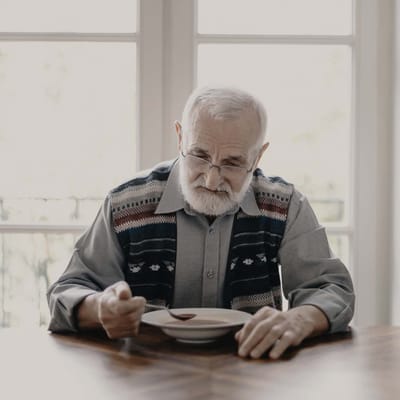 Elderly man sitting at a table with a bowl.