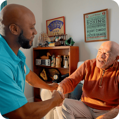 A caregiver and resident shaking hands in a cozy interior.