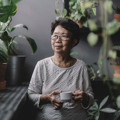 Senior woman enjoying a cup in a plant-filled interior.