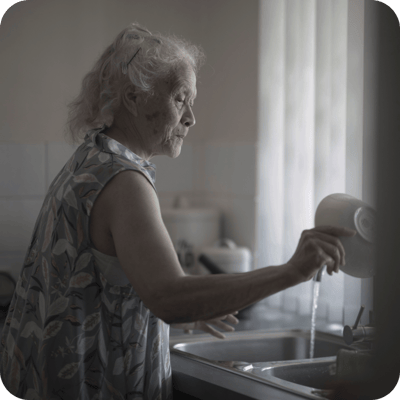 Elderly woman washing dishes at the sink.