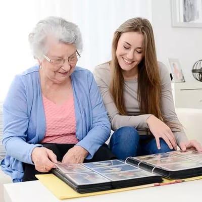 Senior woman and young adult looking at a photo album together.