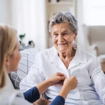 Smiling elderly woman interacting with caregiver indoors.