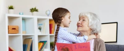 Child with a drawing embraces an elderly woman.