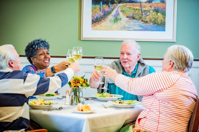 Residents enjoying a meal and toasting at a dining table.