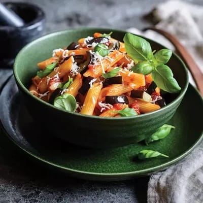 A bowl of pasta with vegetables and basil.